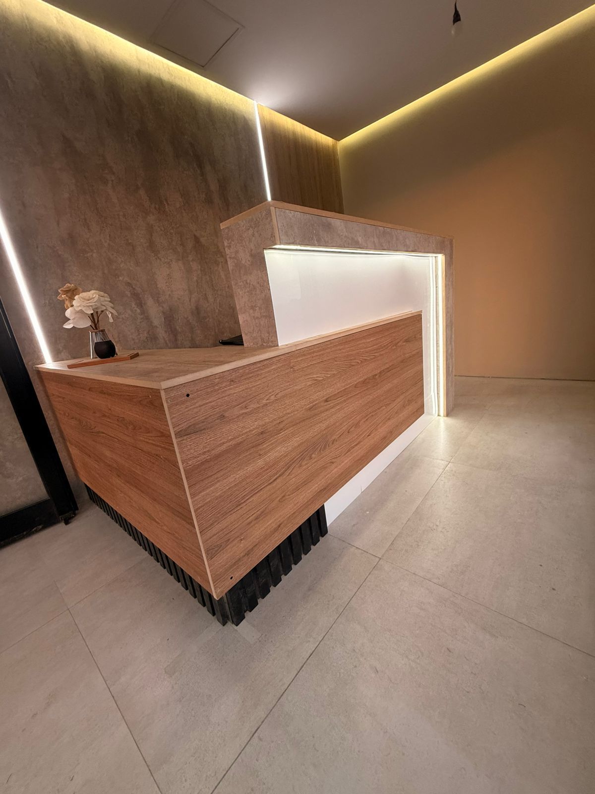 Mostrador de recepción con detalles en madera y blanco, iluminado por luz cenital, en un interior moderno.