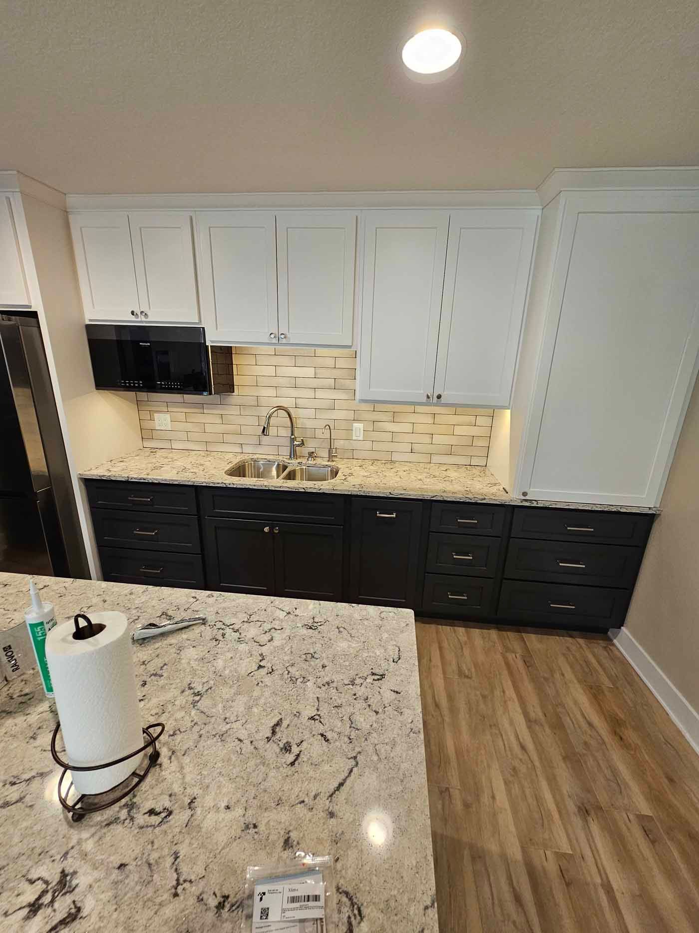 A kitchen with black cabinets , white cabinets , granite counter tops , a sink and a microwave.