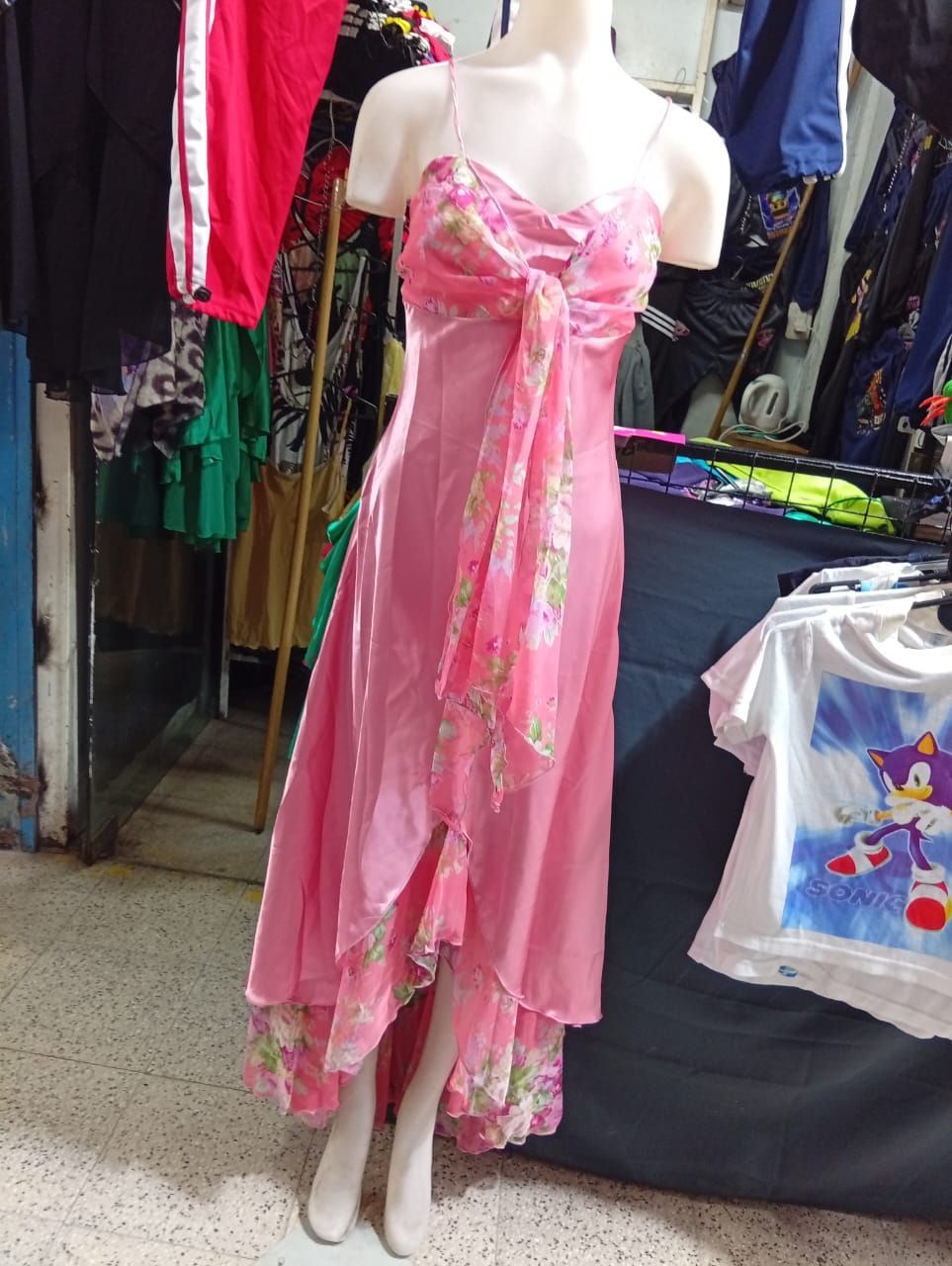 Vestido rosa sobre un maniquí en una tienda; con un lazo en el corpiño y una superposición de tela floral.