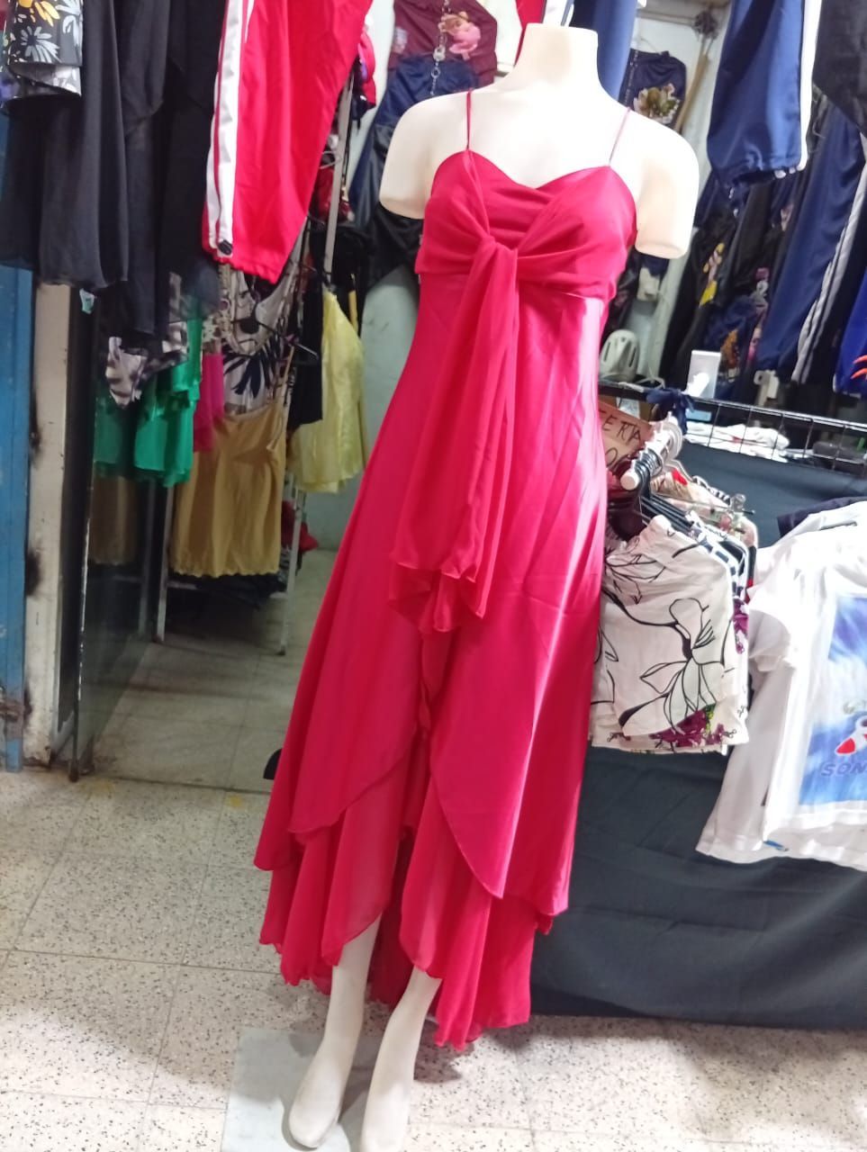 Vestido rosa sobre un maniquí en una tienda; con un lazo en el corpiño y una superposición de tela floral.