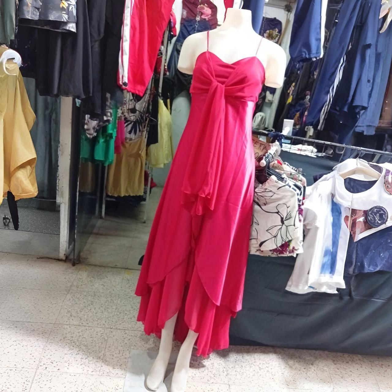 Vestido rosa en un maniquí en una tienda de ropa, con otras prendas visibles al fondo.