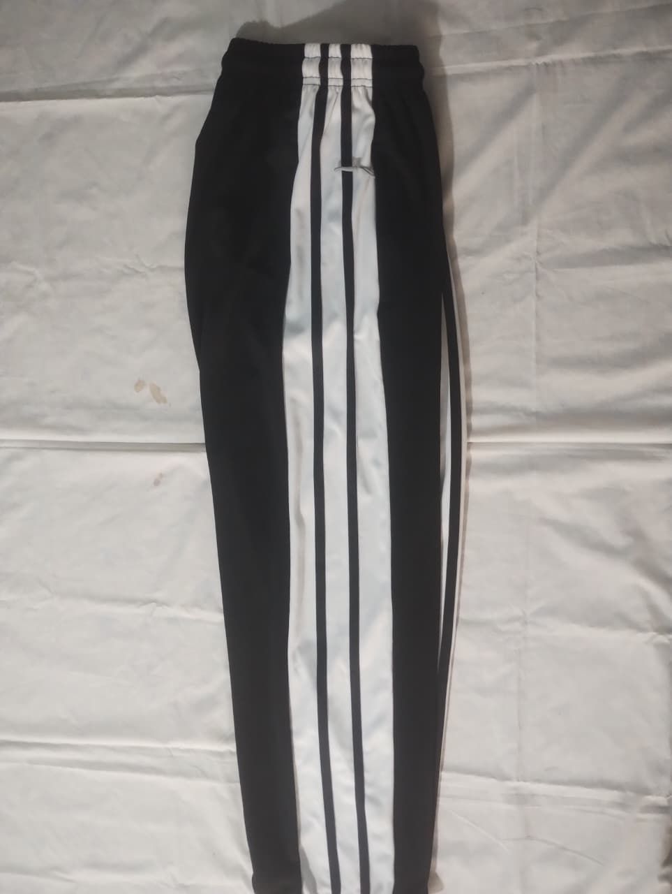 Tres pantalones deportivos Adidas: azul con rayas rojas, blanco con rayas negras y azul marino con rayas blancas.