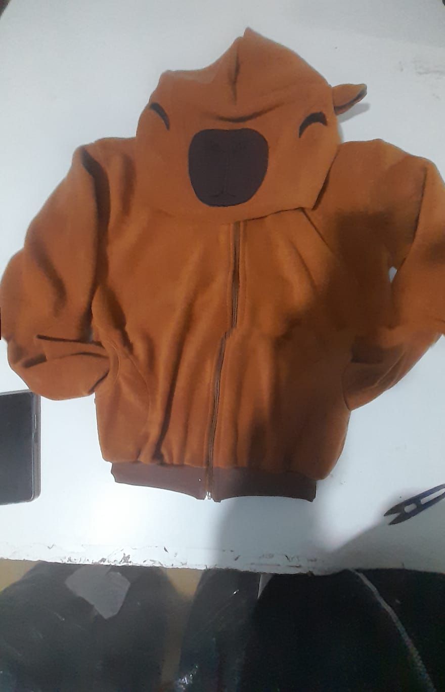 Sudadera marrón con capucha y cara de oso estampada, cerrada con cremallera sobre una superficie blanca.