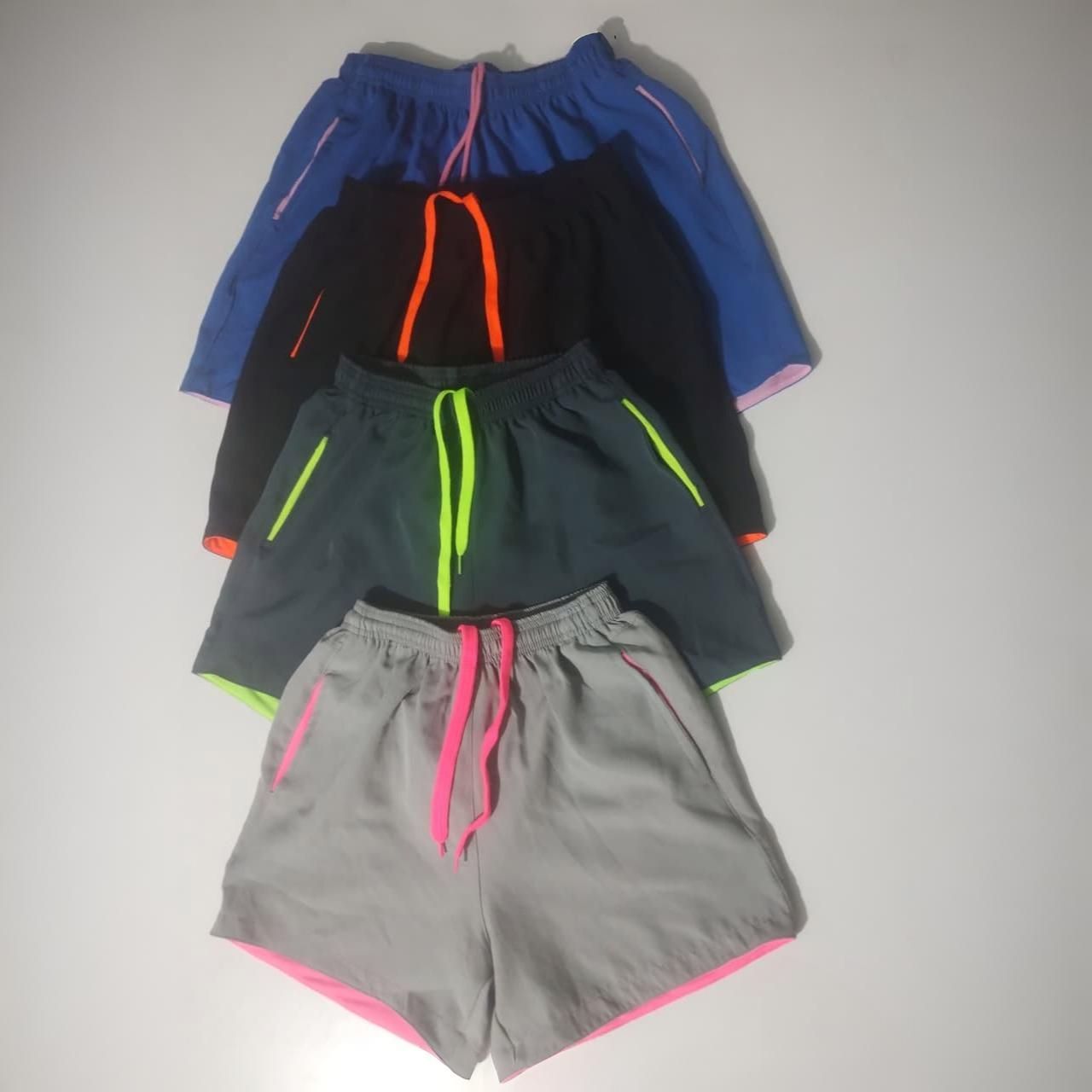 Cuatro pares de pantalones cortos deportivos en azul, negro, verde y gris, con ribetes de colores brillantes .