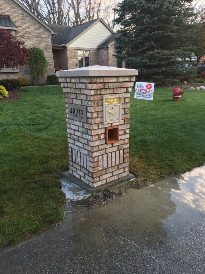 A brick mailbox is sitting in front of a house.
