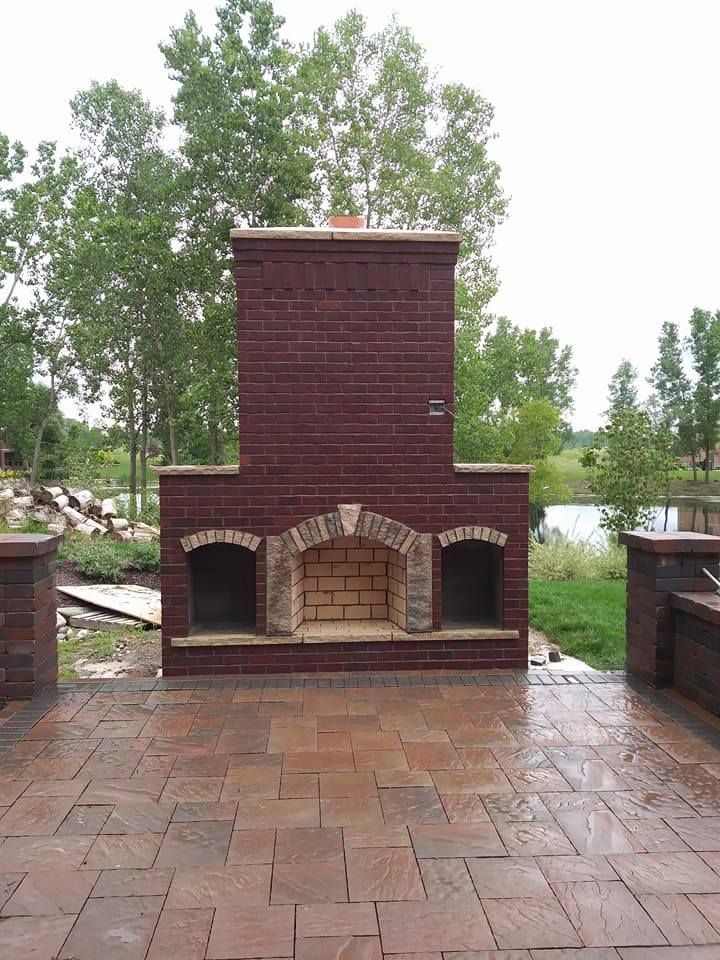 Brick outdoor fireplace with arched firebox and two side openings on a brick patio.