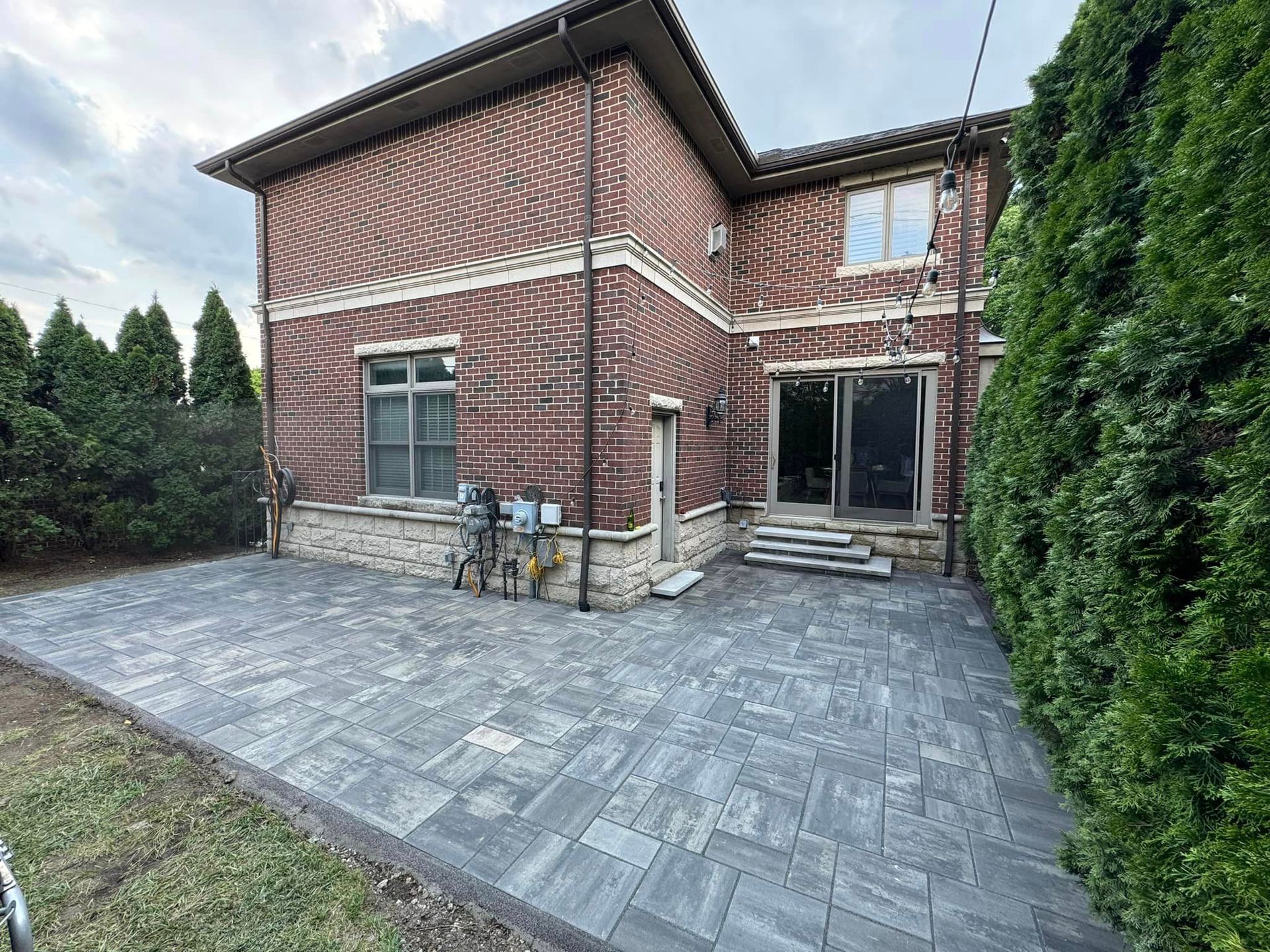 Brick home with gray patio and lush green bushes.