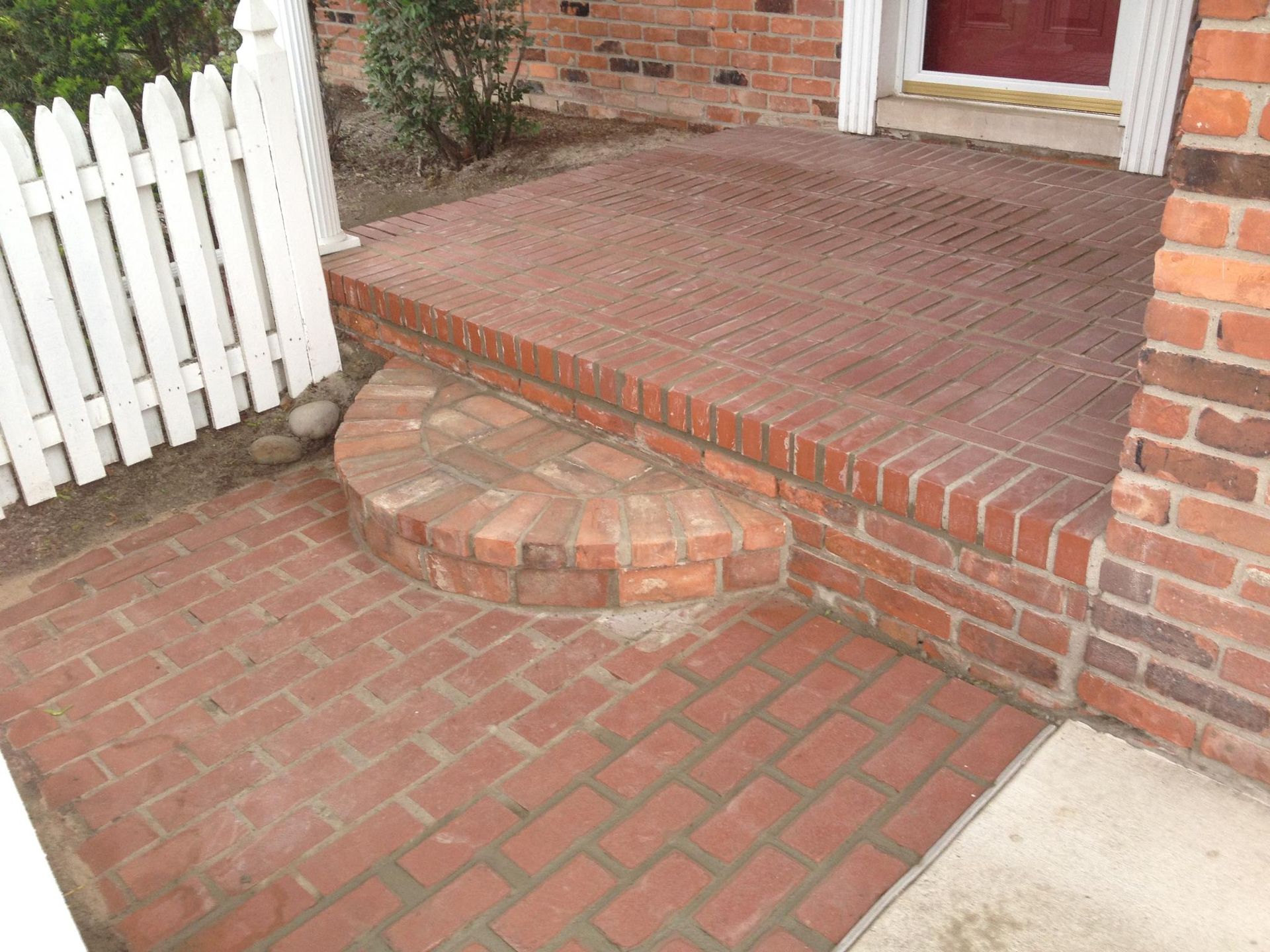 A brick walkway with a white picket fence in the background