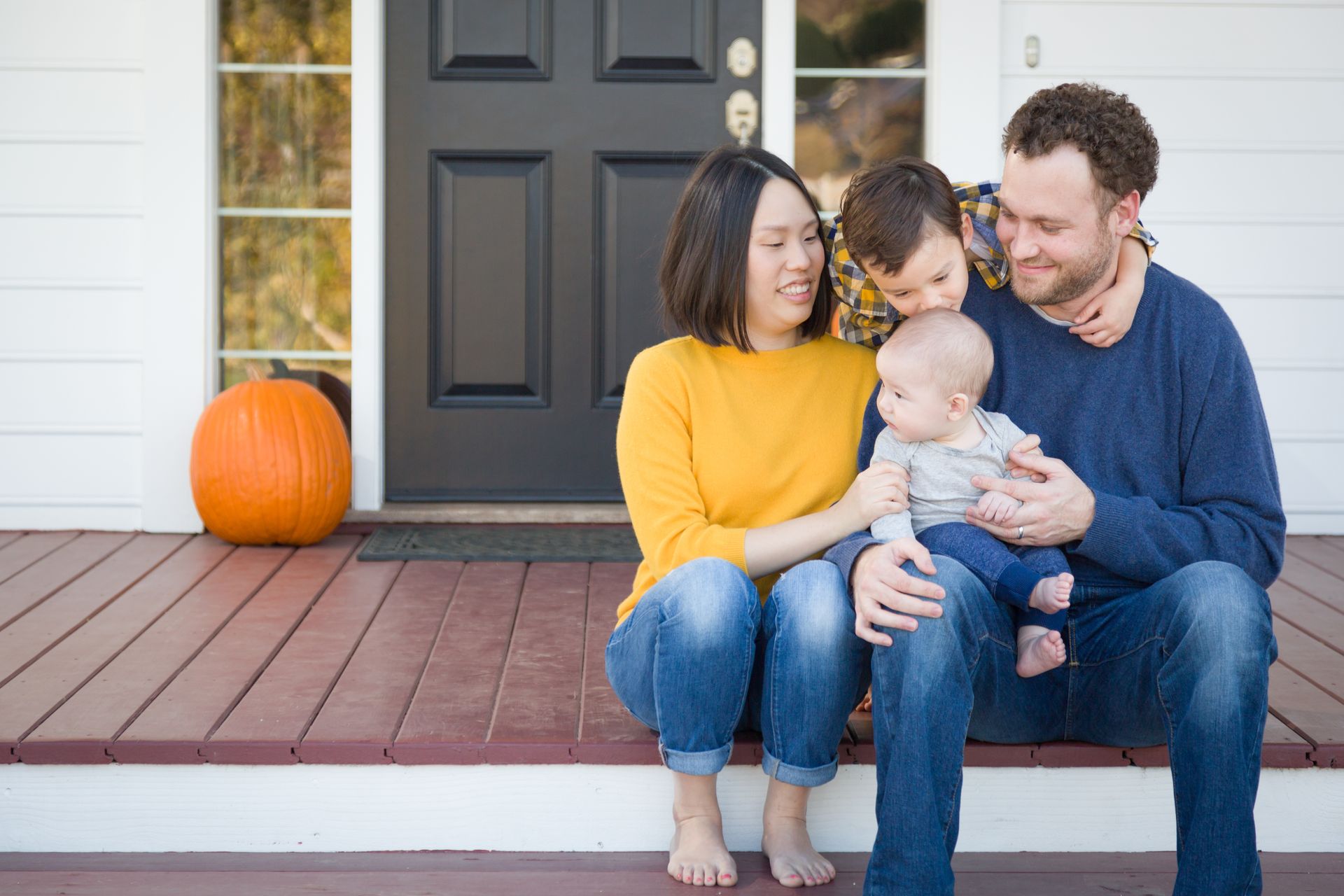 Family of four sitting on porch with pumpkin.