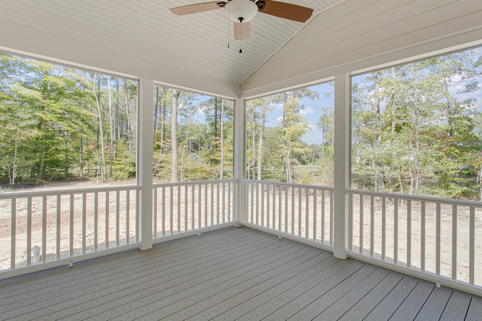 Screened porch with fan overlooks wooded yard and sandy ground.