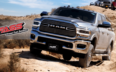 A silver ram truck is driving down a dirt road.