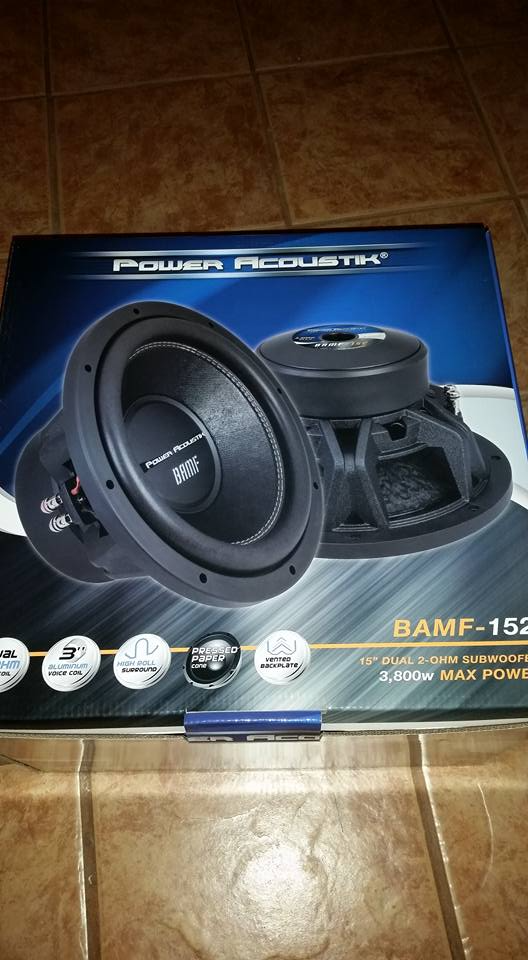 A pair of subwoofers in a box on a tiled floor.