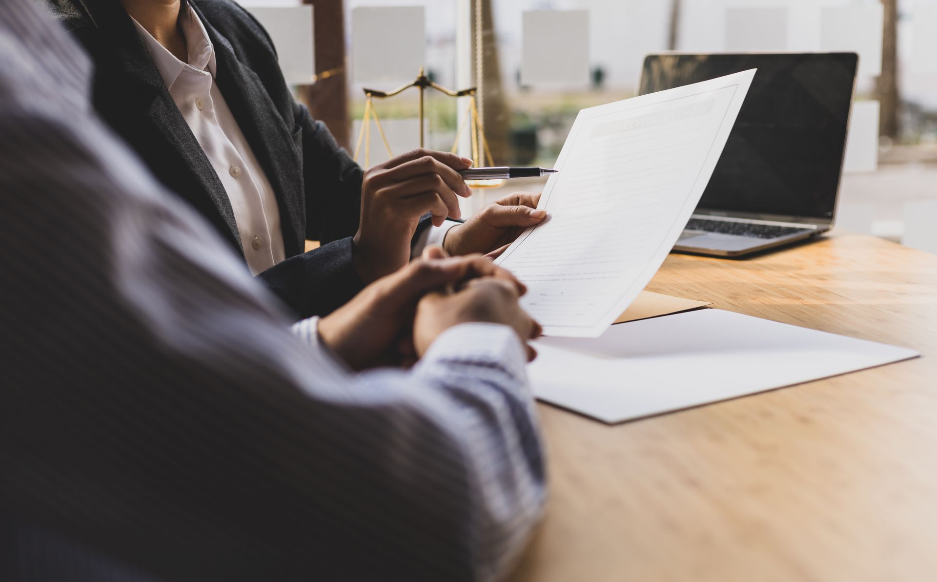 Two people reviewing documents at a table; one points to the paper near a laptop.