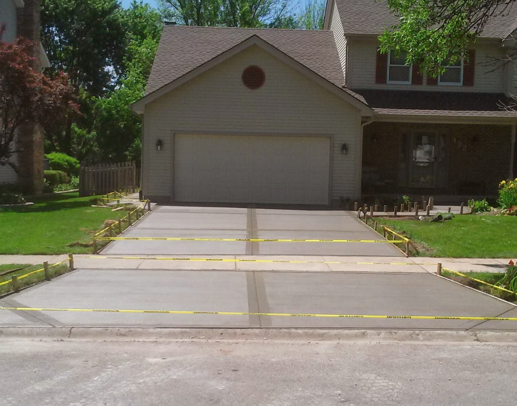 Newly poured concrete driveway in front of a house, blocked off with yellow caution tape.