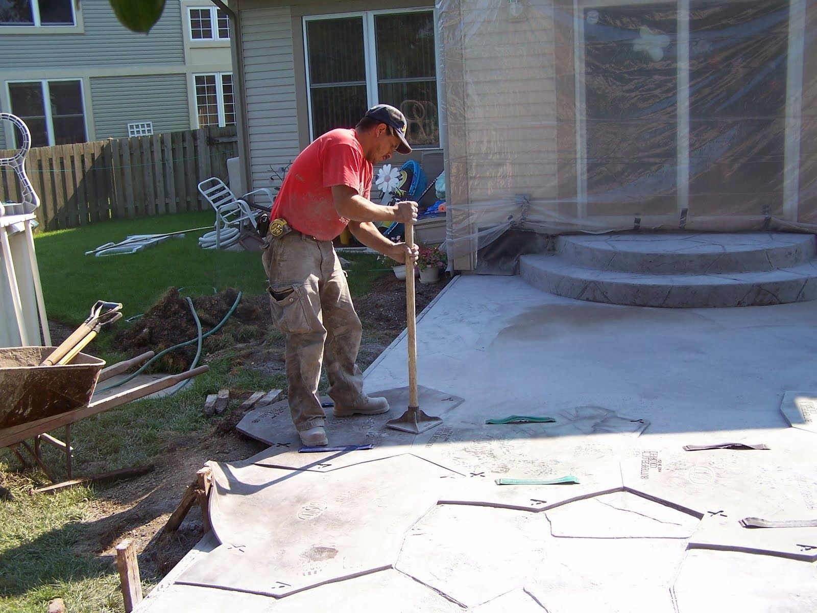 A man in a red shirt is working on a patio with a shovel.