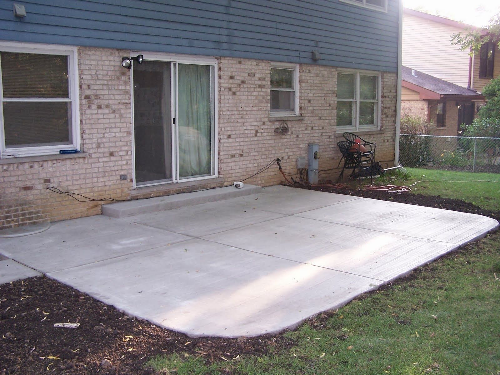 Concrete patio next to a house with a sliding glass door and windows. Mulch borders the patio.