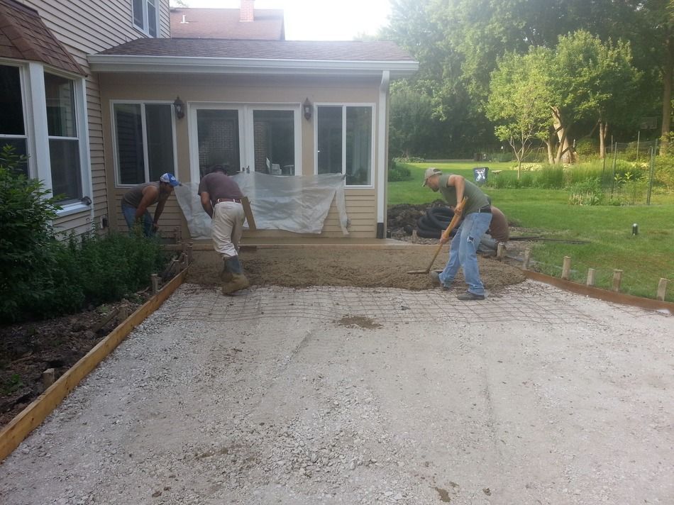 Two men are working on a driveway in front of a house.