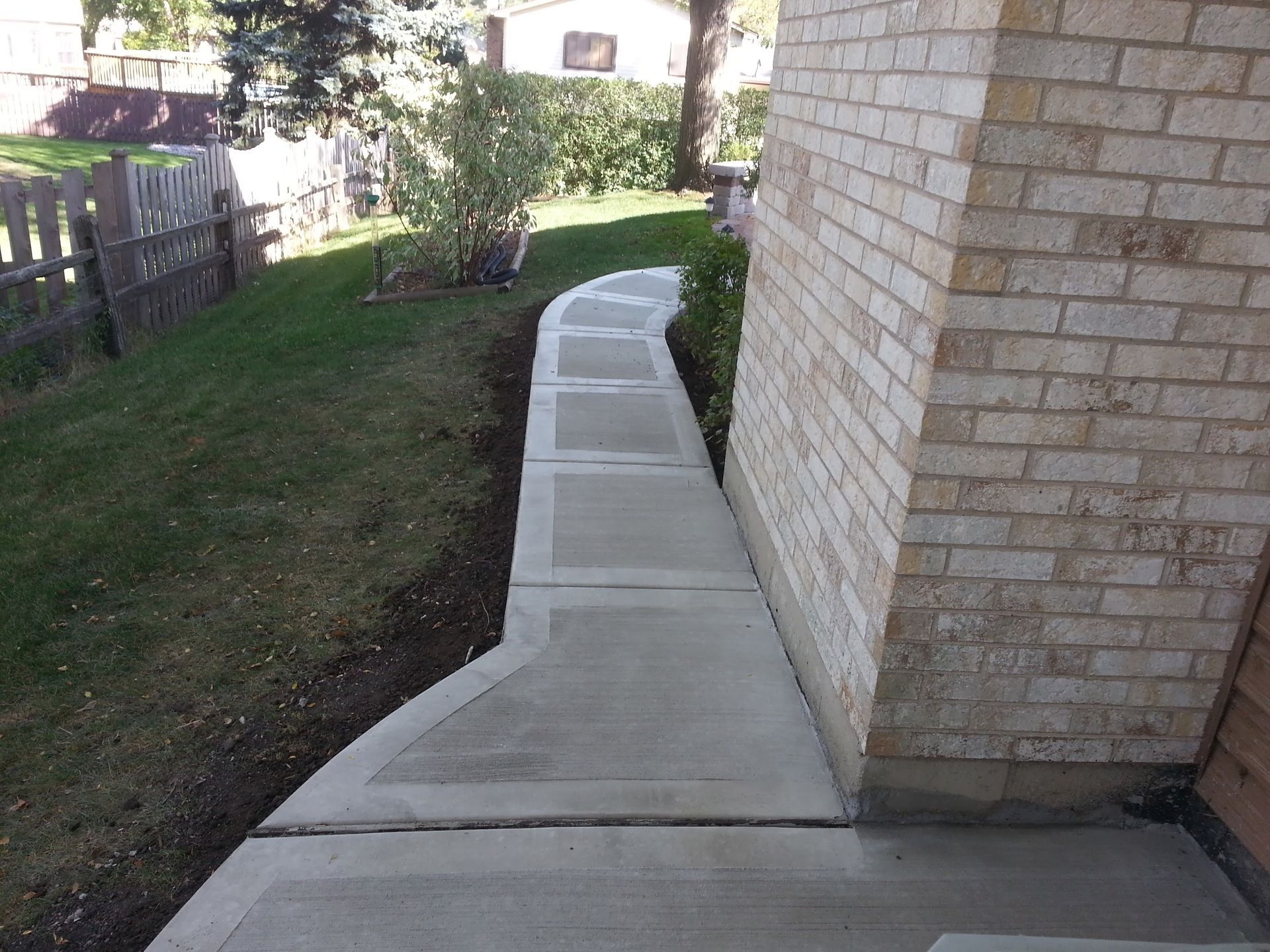 Concrete walkway beside a brick building and grass lawn.
