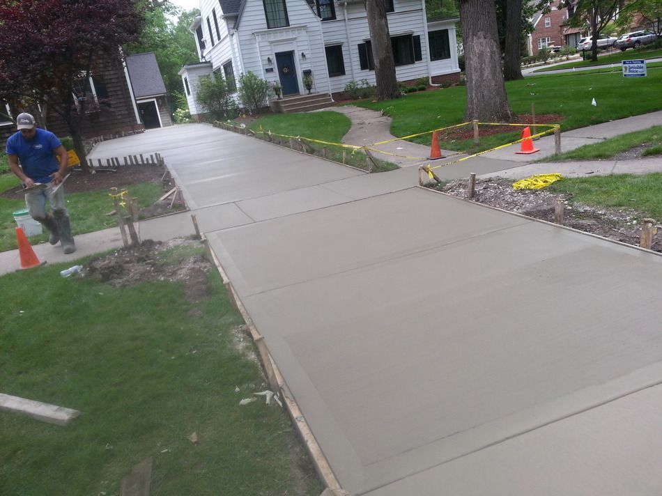 A man is standing on a concrete sidewalk in front of a house.