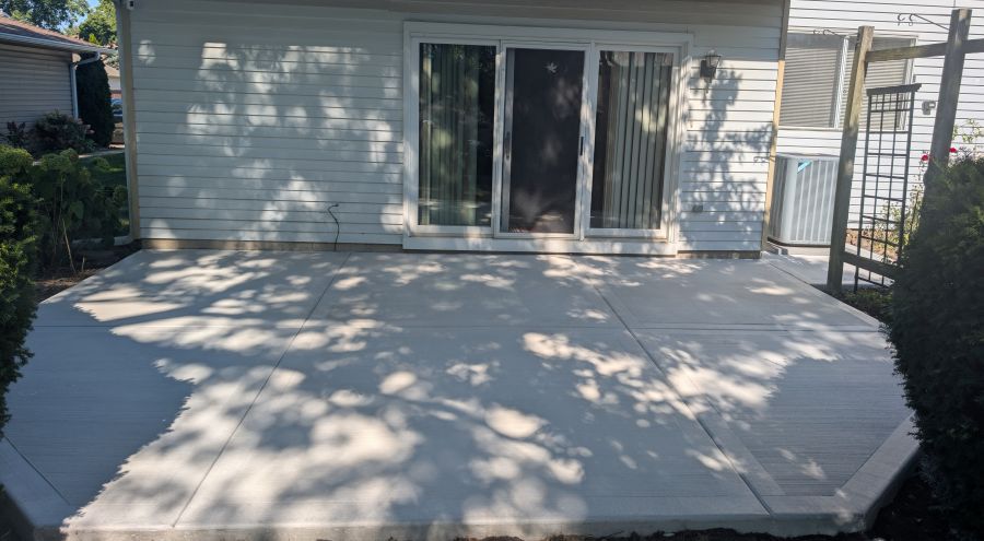 Concrete patio outside a house with a sliding glass door. Shadows of trees are cast on the patio.