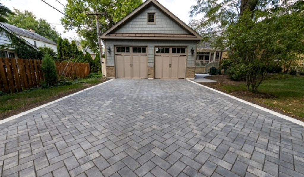 Newly paved concrete driveway leading to a brick house with large windows and a wooden fence.