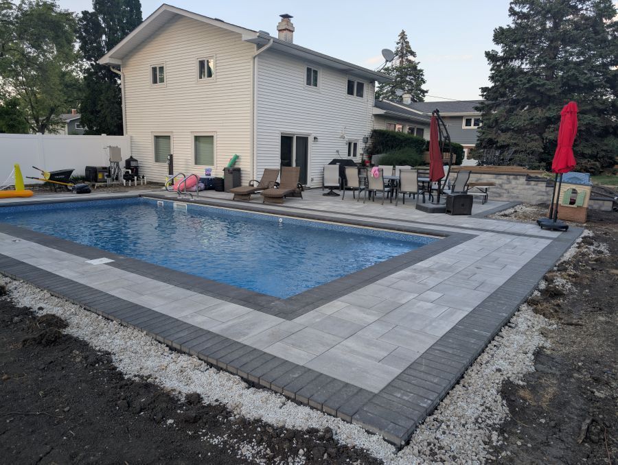 Backyard with swimming pool, light gray brick paving stones, white gravel, and a two-story white house.