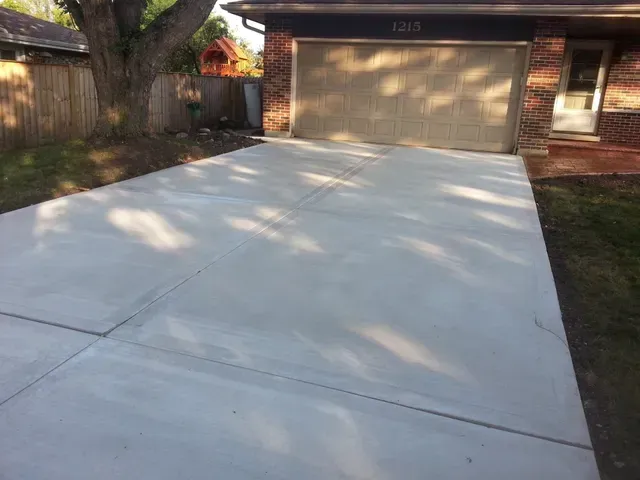 A concrete driveway leading to a garage with a brick house in the background.