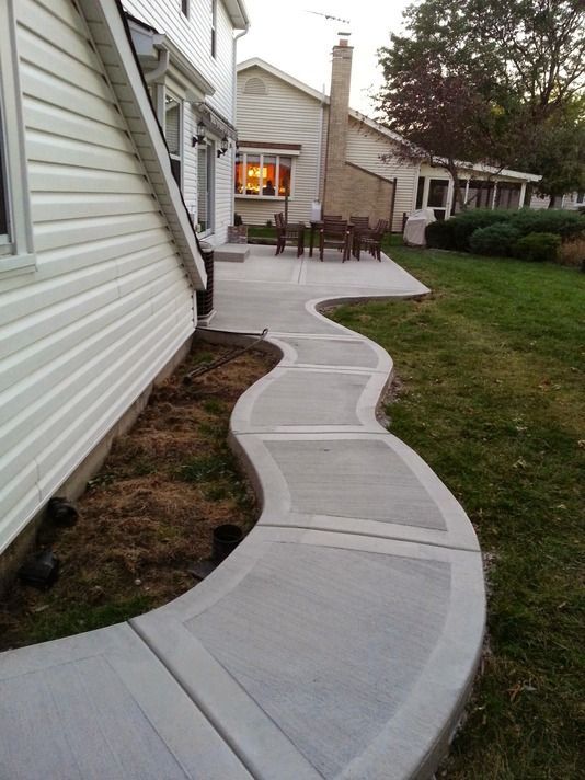 A concrete walkway leading to a patio in front of a house