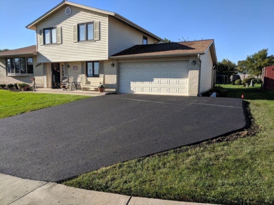 Black asphalt driveway in front of a beige two-story house with a two-car garage.