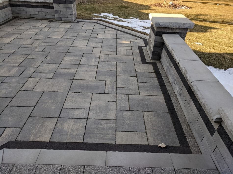 A brick patio with a black border and a bench