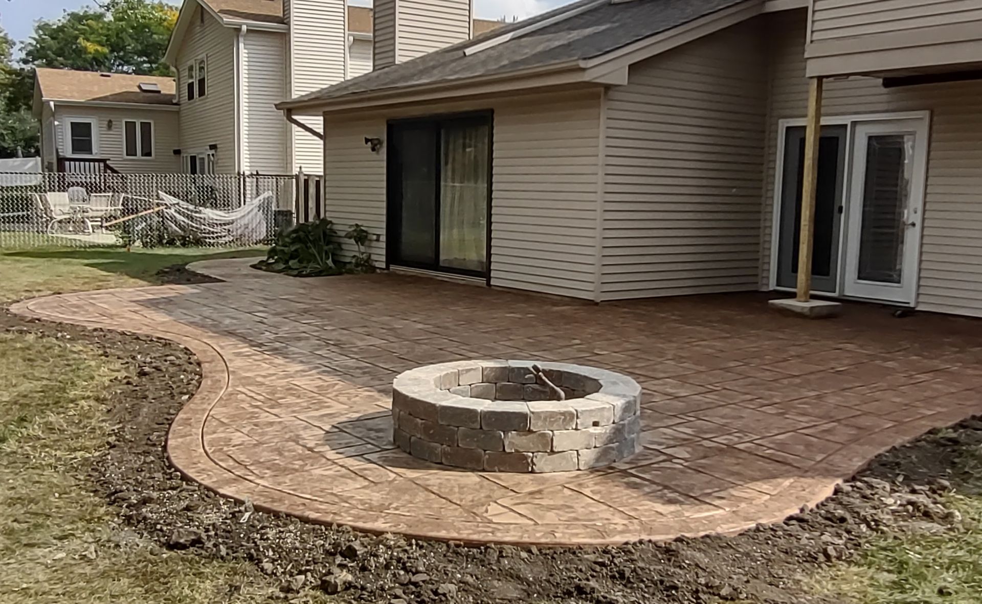 A fire pit is in the middle of a patio in front of a house.