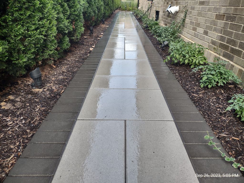 Concrete walkway beside a brick building and grass lawn.