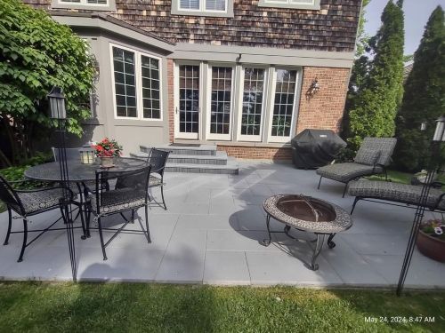 Patio with gray brick paving stones, seating, and fire pit in front of a brick house.