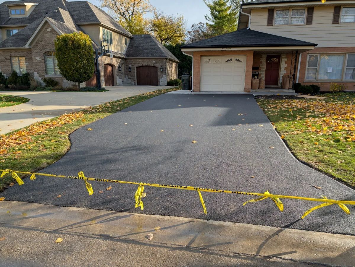 Newly paved asphalt driveway with yellow caution tape, in front of a house.