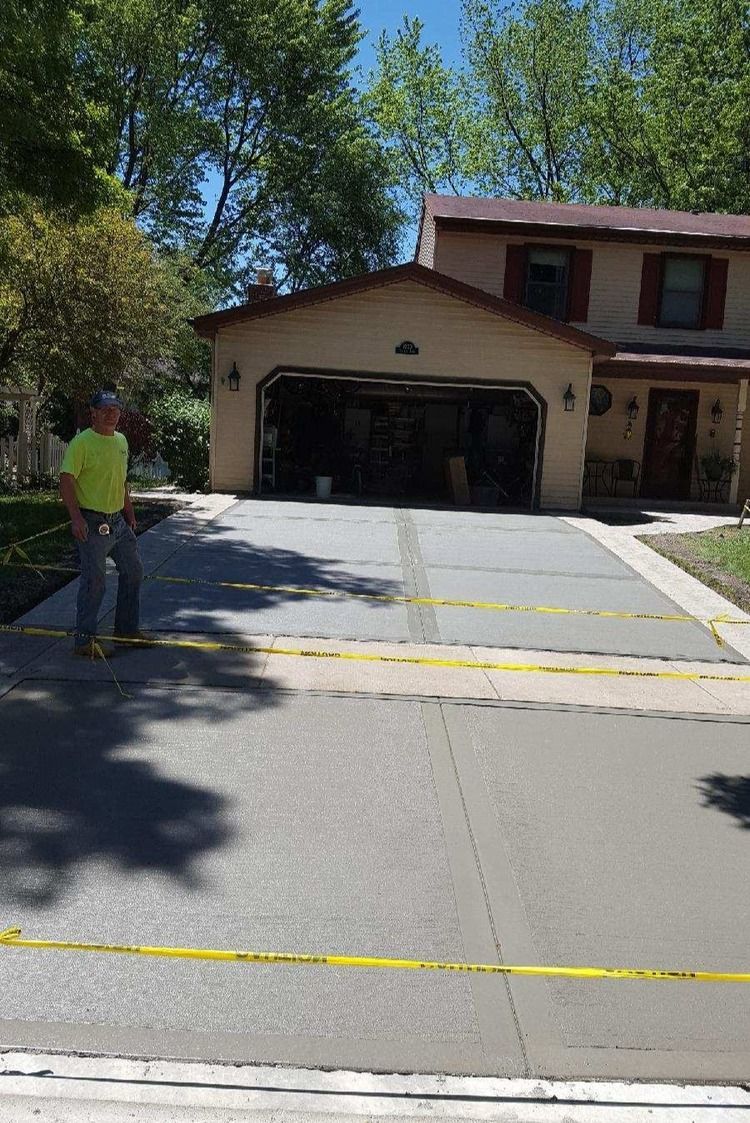 A man is standing in front of a house with a concrete driveway.