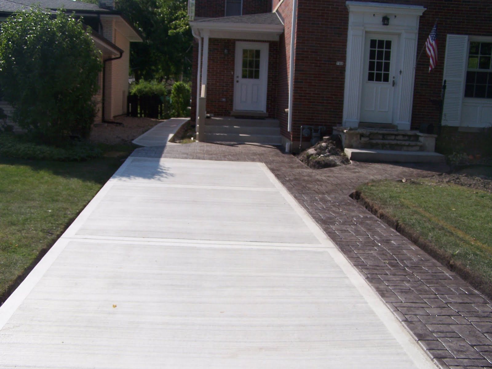 Newly poured concrete driveway leading to a brick house with a front door and porch.
