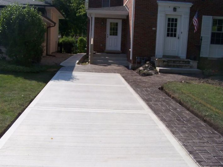 Newly poured concrete driveway leading to a brick house with a front door and porch.