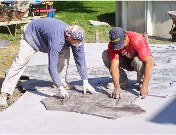 Two men are working on a concrete surface and one is wearing a hat that says eagles