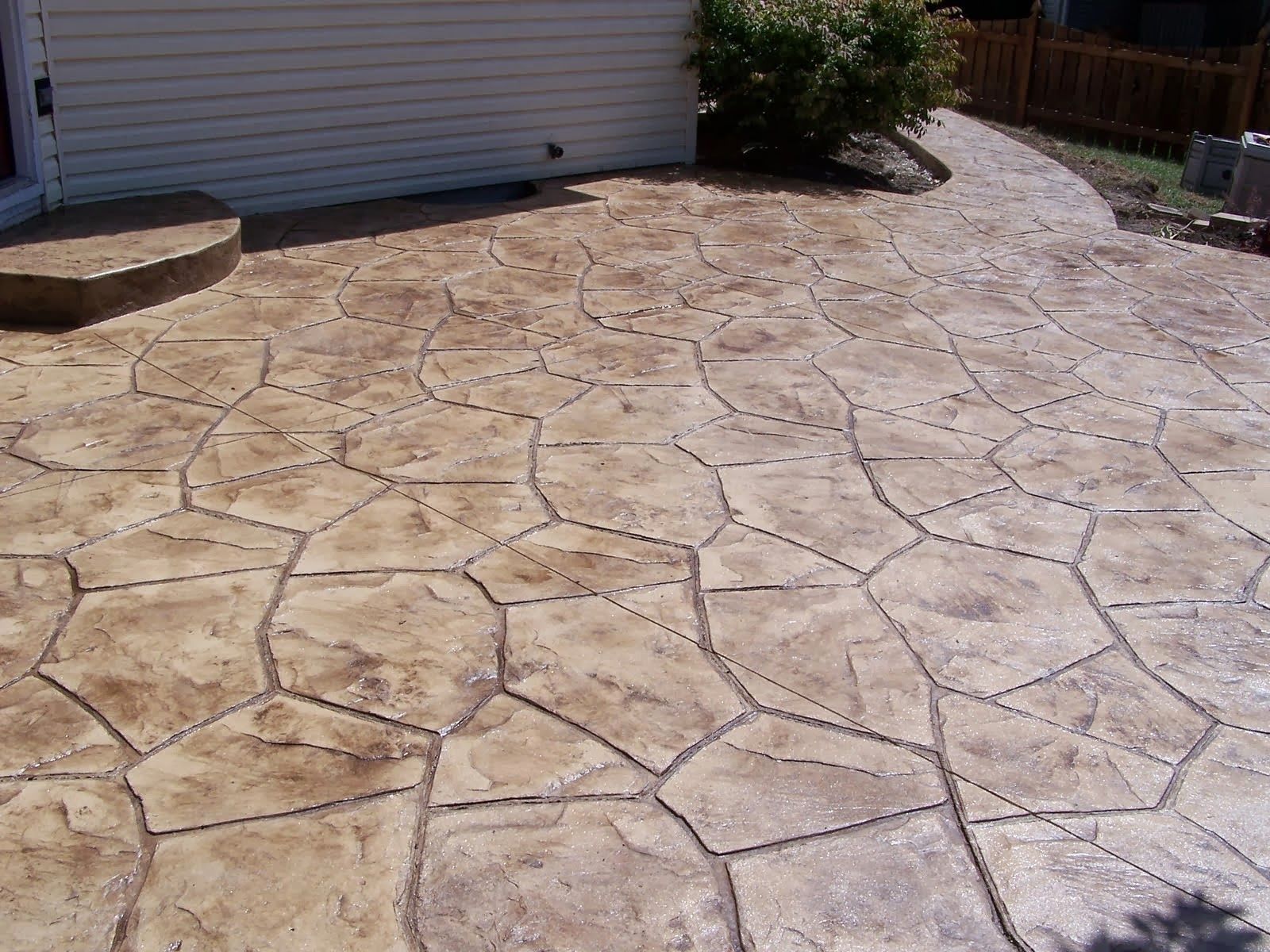 Stamped concrete patio with a stone-like pattern, in brown and gray hues, leading to a pathway and a building.