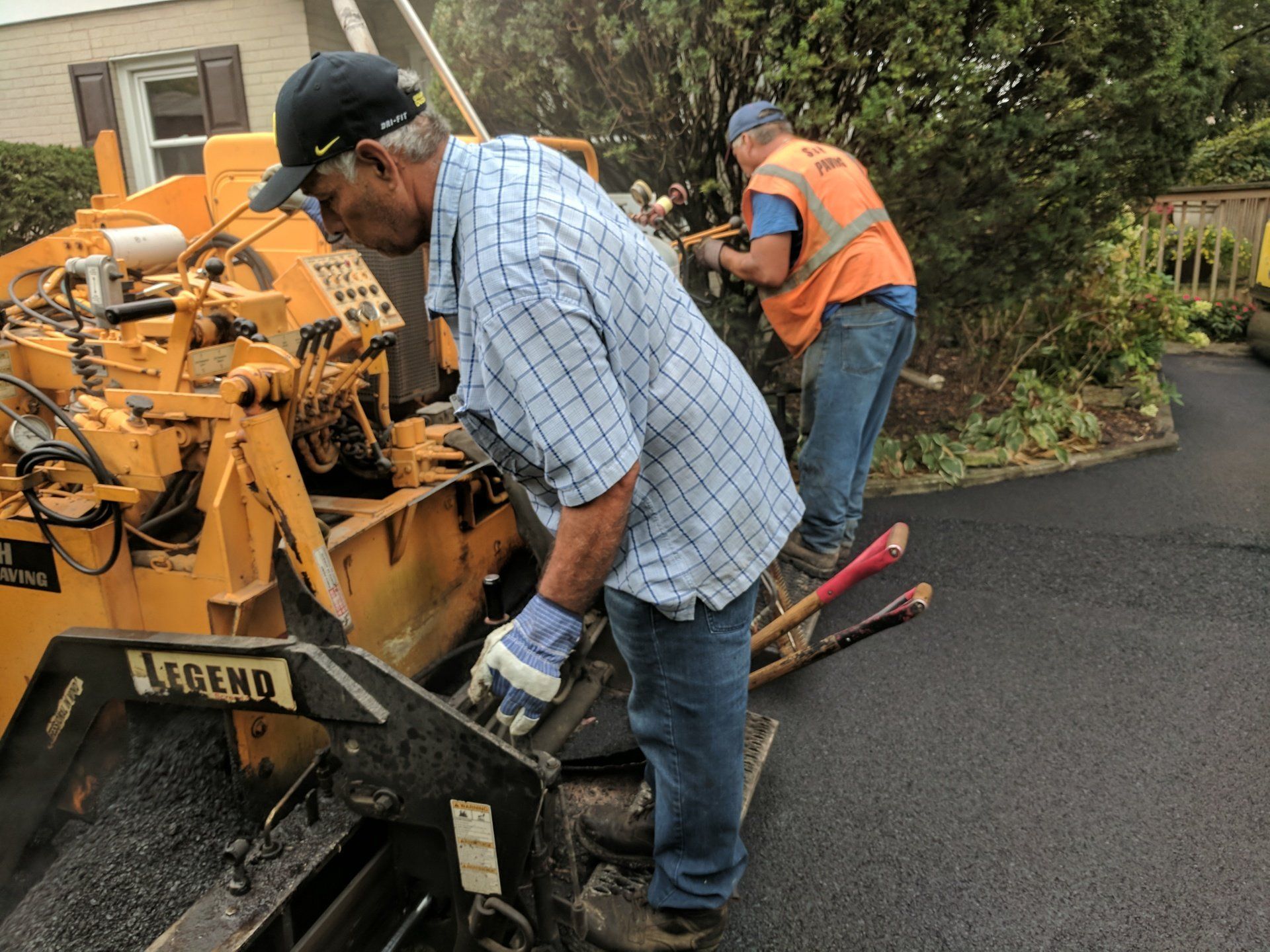 A man is working on a brick driveway in front of a brick house.