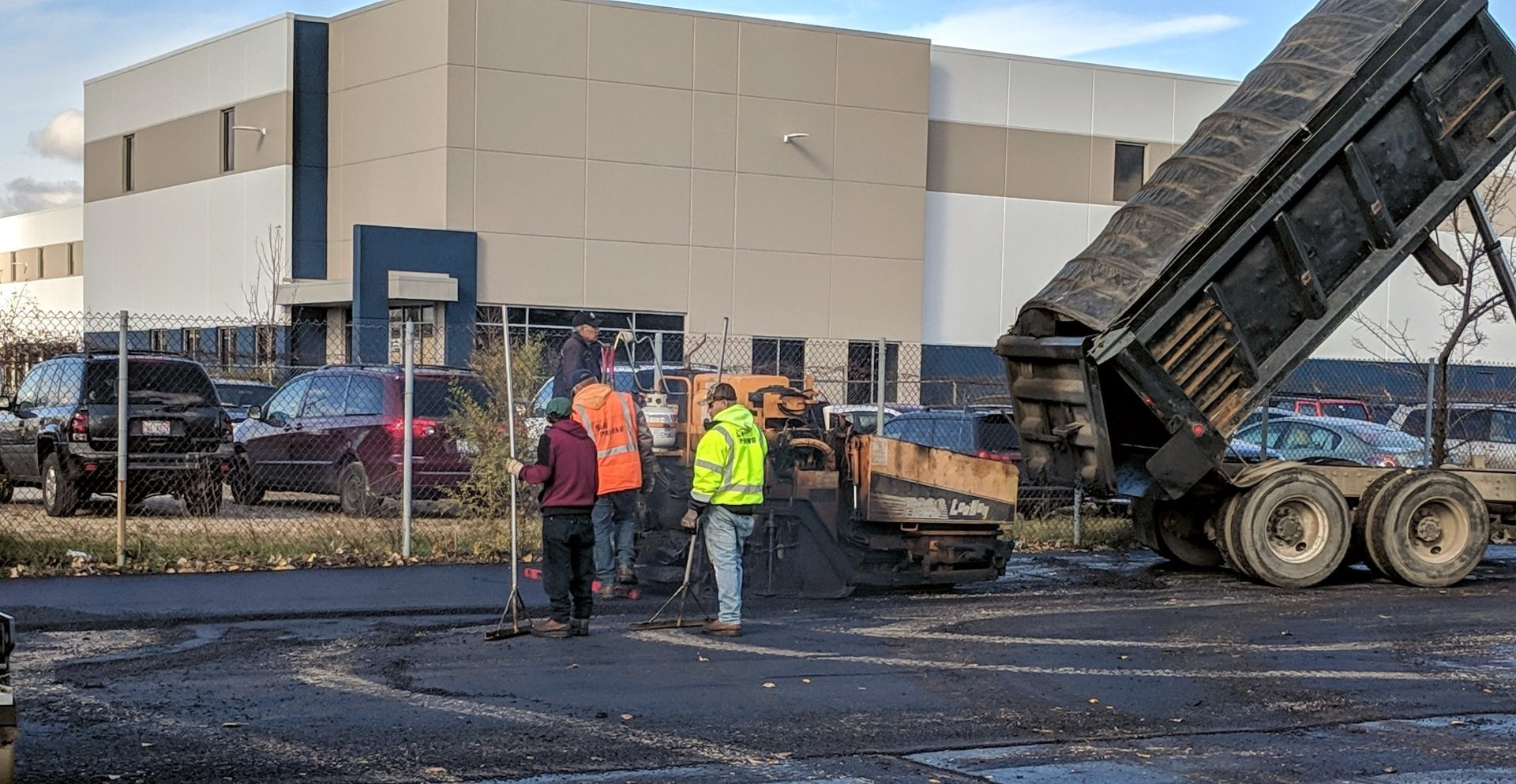 A dump truck is being loaded with asphalt in a parking lot.