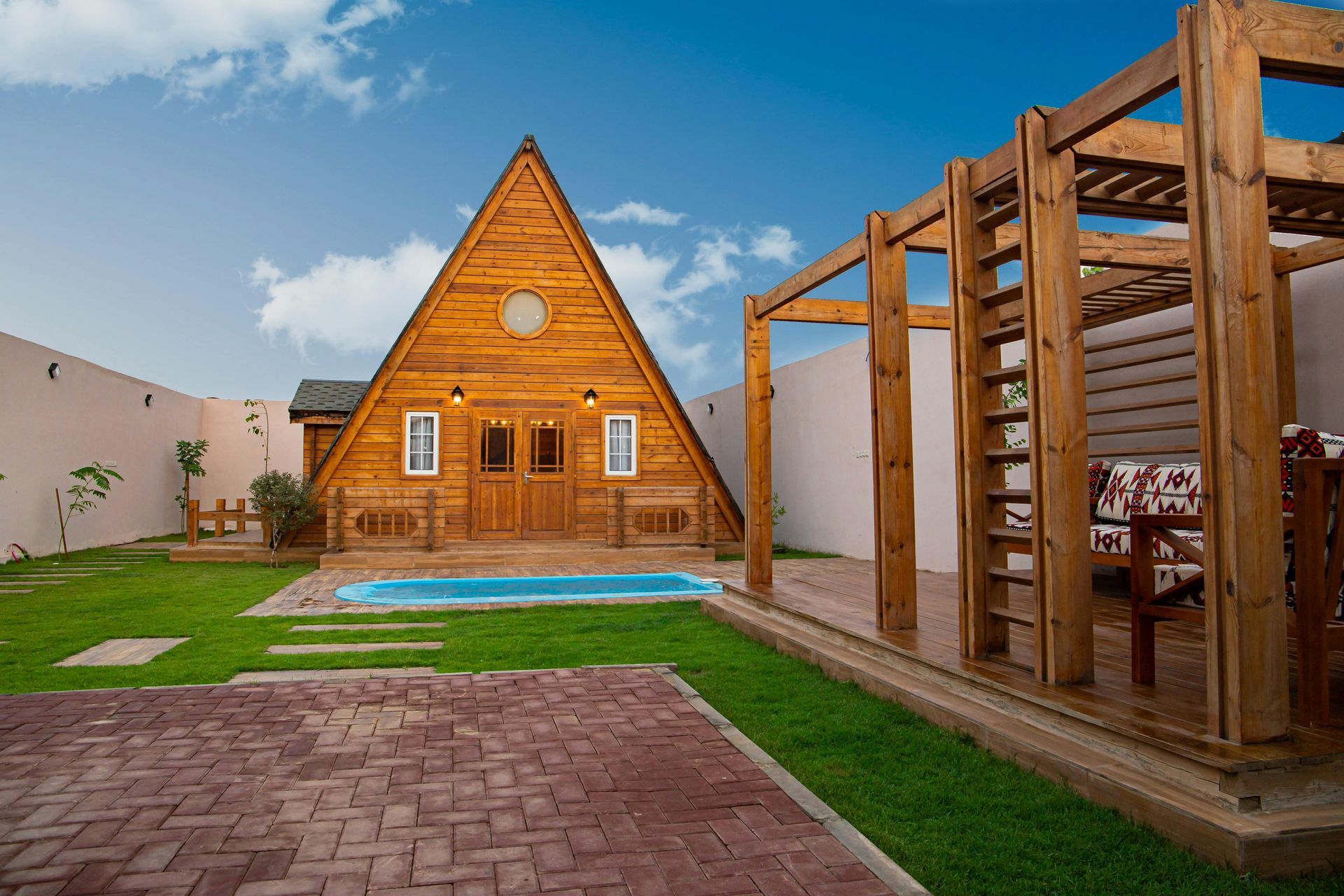 Wooden A-frame cabin with a pool and pergola in a yard.