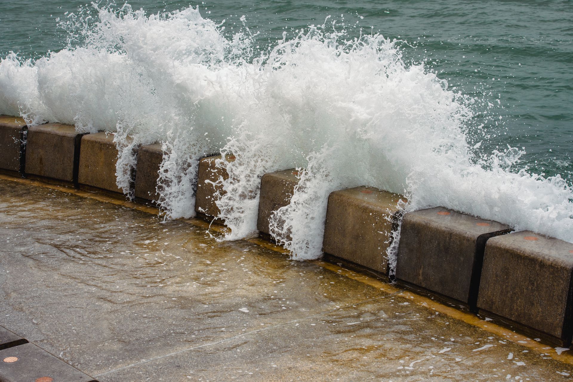 Waves crash against seawall, splashing water over the top.