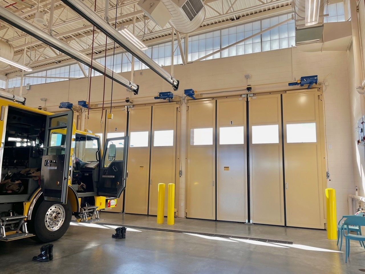 A yellow fire truck is parked in a garage with its doors open.