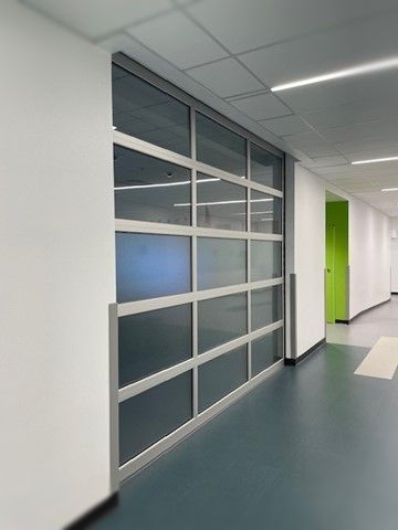 A long hallway with a glass wall and a green door.