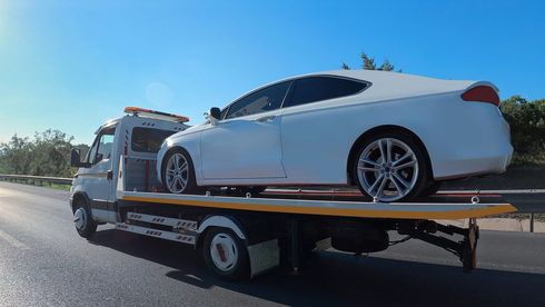 A white car is being towed by a tow truck