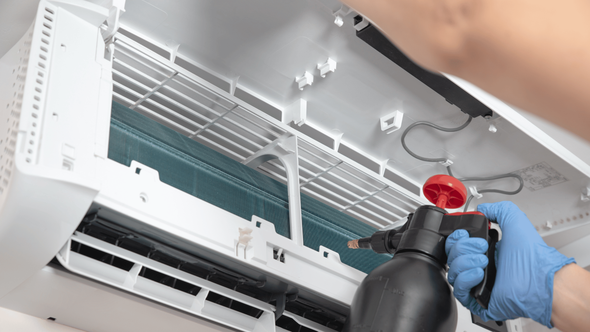 A person is cleaning an air conditioner with a spray bottle.