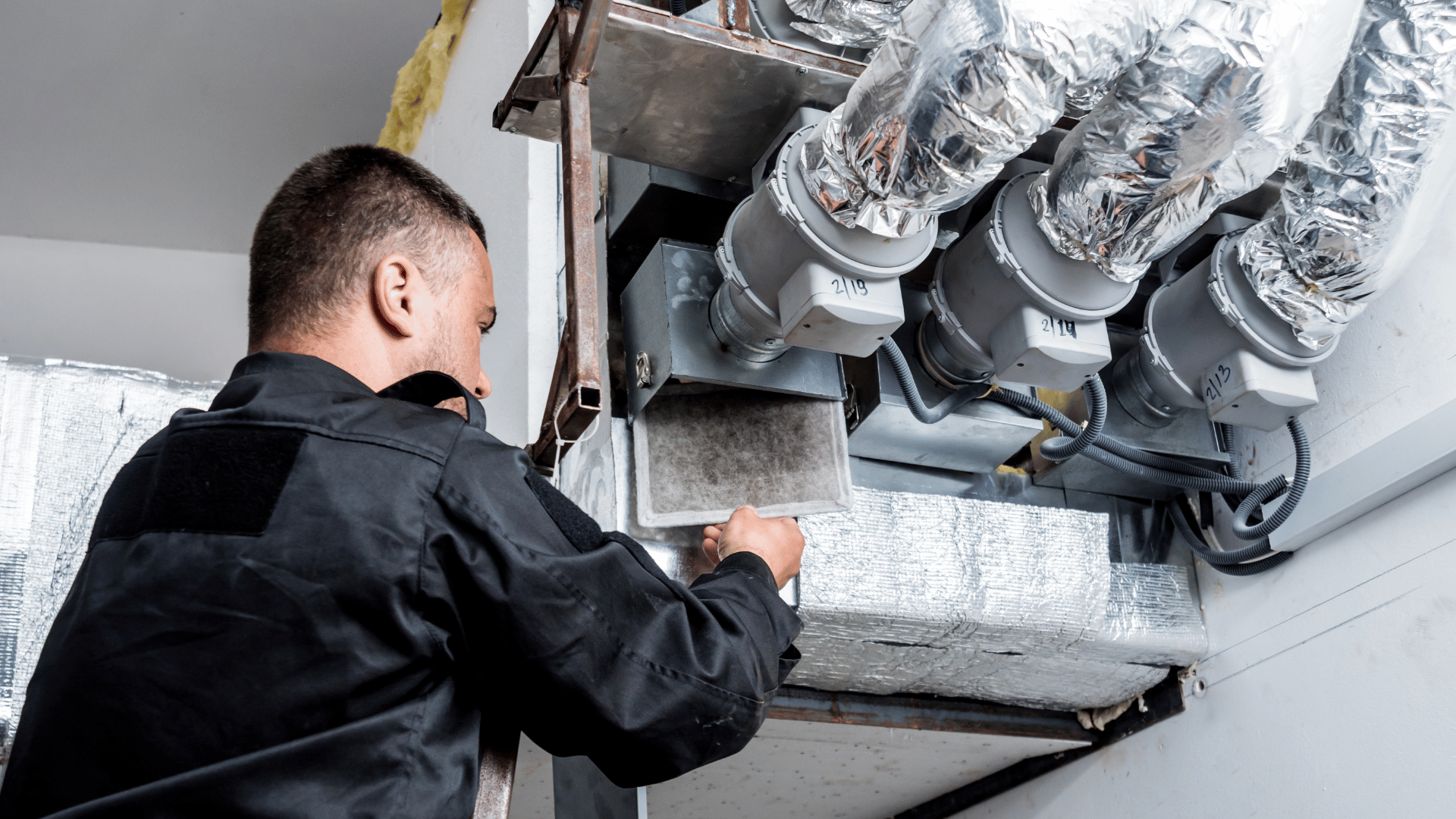 A man is working on a ventilation system in a building.