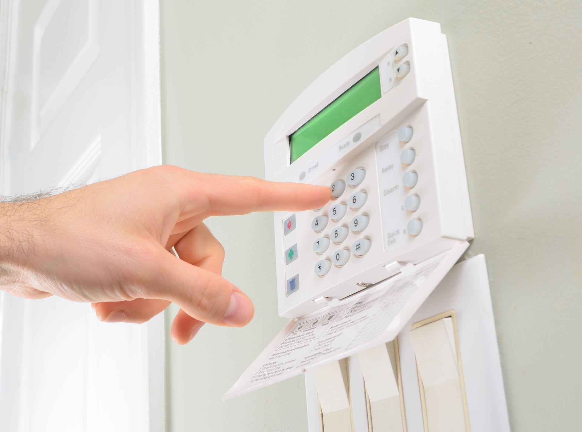 A hand presses a button on a white wall-mounted home security alarm keypad.
