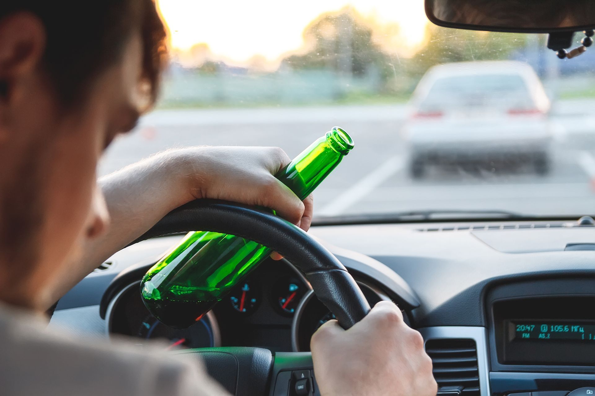 Man driving with two beer bottles in his lap, looking down at the steering wheel.
